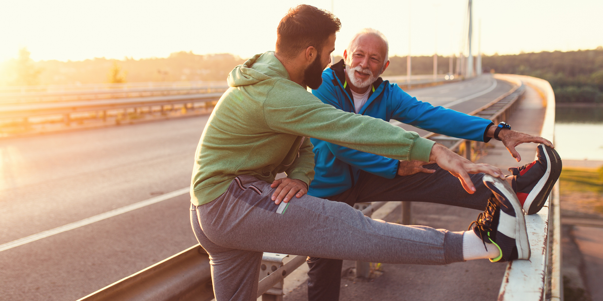 younger man and older man in sweats prop their legs on a wall to stretch