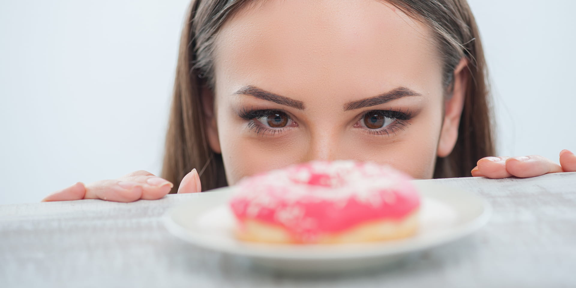 girl peeking over table edge at frosted donut