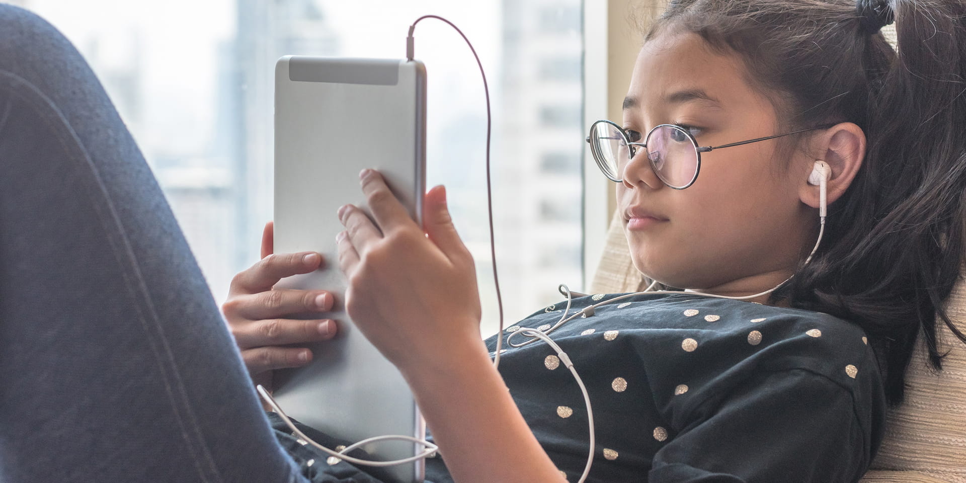 little girl on her bed with earbuds looking at her tablet