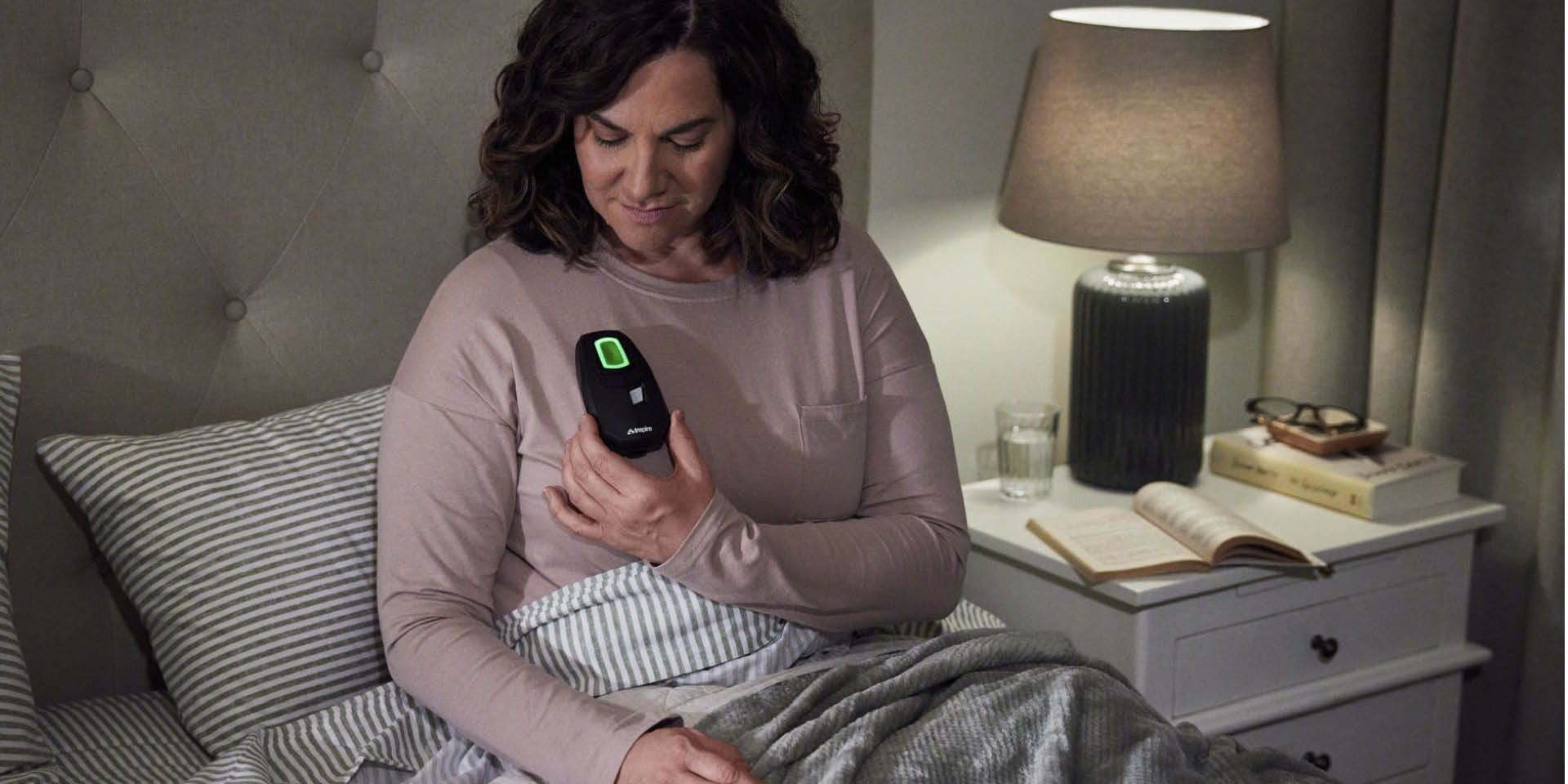 Woman sitting up in bed holding device over her chest | Doylestown Health