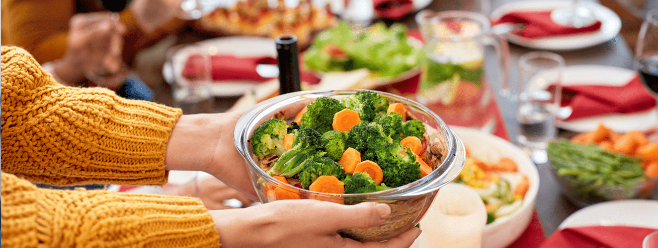 Woman holding bowl full vegetables over served dinner table with tasty homemade food and preparing for celebrating holidays and birthday with family | Doylestown Health