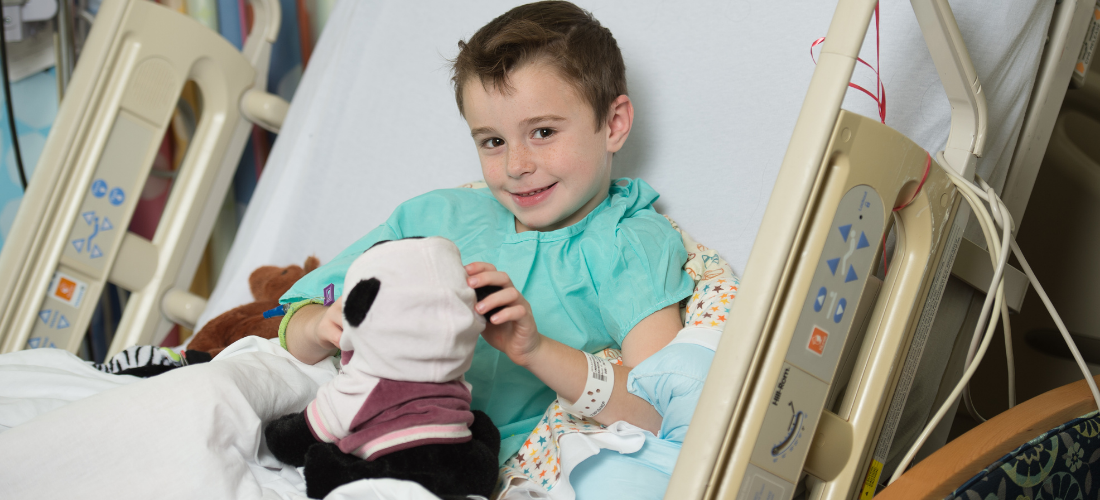 Young child in an hospital bed plays with a Panda bear | Doylestown Health